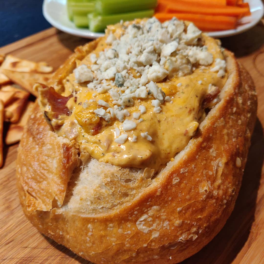 Smoked buffalo chicken dip in a hollowed sourdough bread bowl, topped with blue cheese crumbles